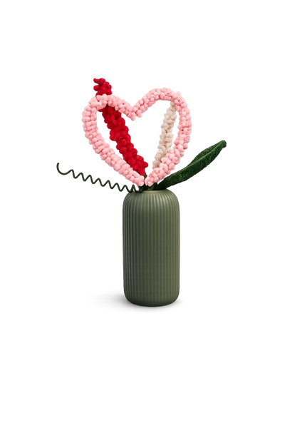 Pink crochet heart stem with a red sprig and a green leaf in a sage green ribbed vase