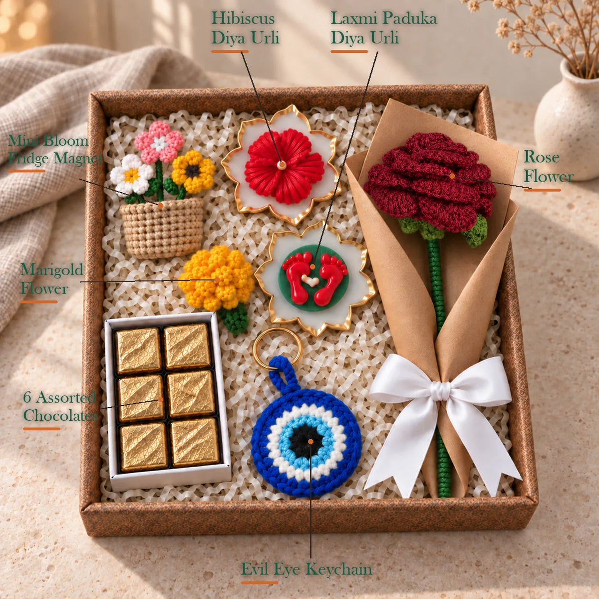 Labelled contents of the Ghar Ki Festive Hamper: rose, evil eye keychain, marigold, magnet, chocolates, 2 urlis